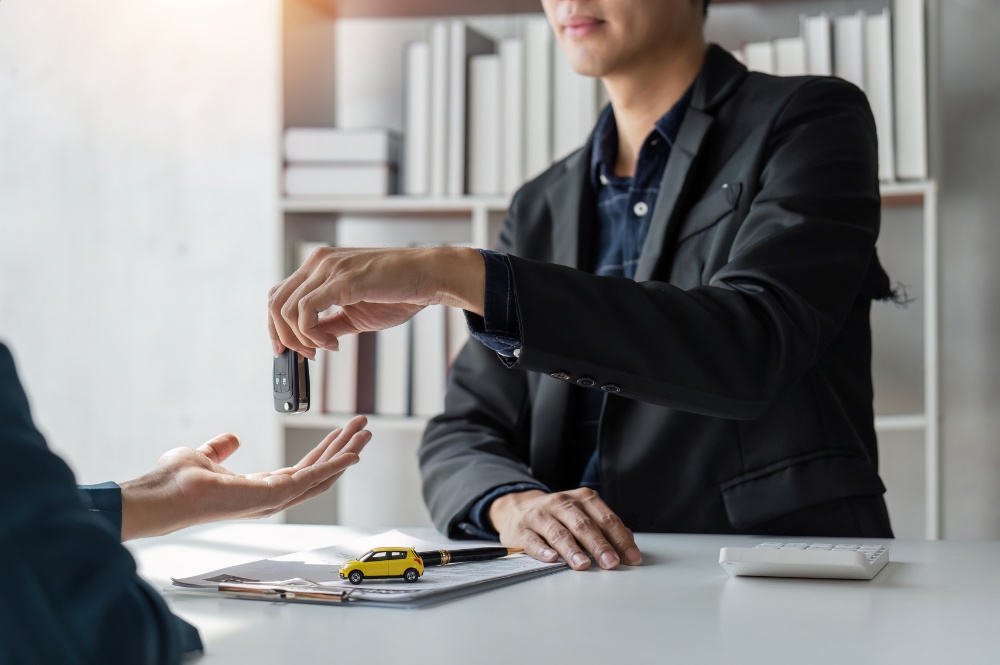 Person handing keys to outstreched hand. There is a minature toy car on the table.